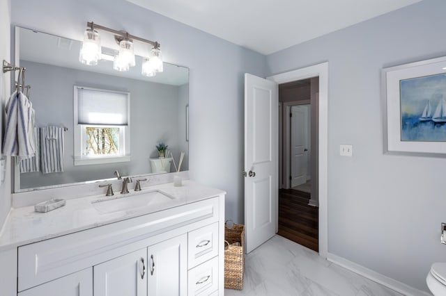 bathroom featuring toilet, marble finish floor, vanity, and baseboards