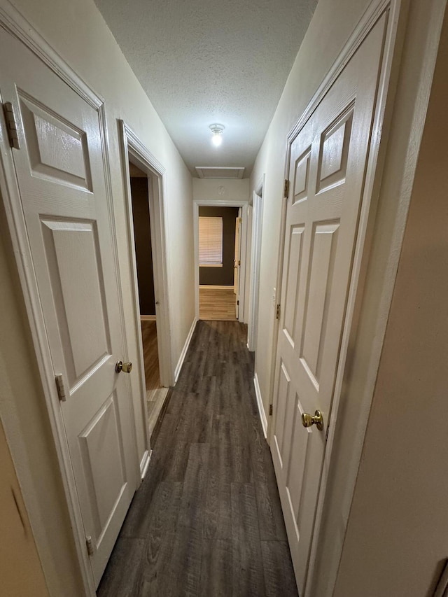 hall with dark wood-style flooring, baseboards, and a textured ceiling