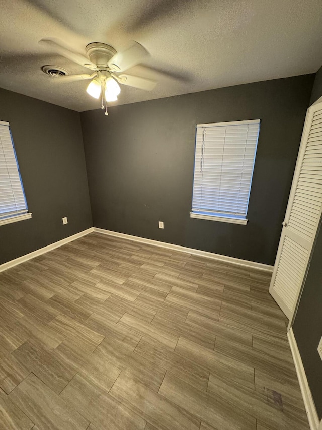 unfurnished bedroom with a textured ceiling, ceiling fan, visible vents, baseboards, and wood finished floors