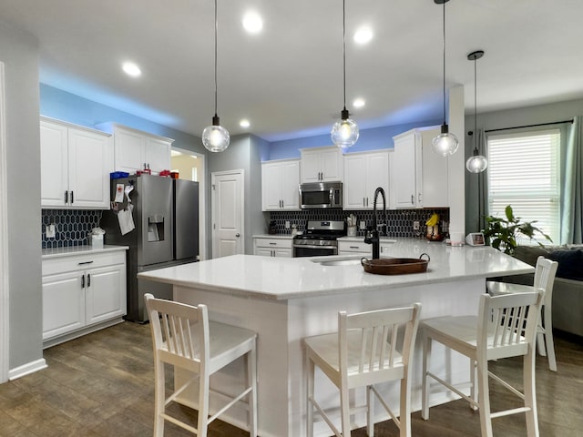 kitchen with white cabinetry, decorative light fixtures, stainless steel appliances, a kitchen breakfast bar, and dark hardwood / wood-style flooring