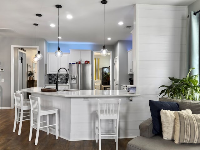 kitchen featuring a kitchen breakfast bar, stainless steel fridge, dark hardwood / wood-style flooring, pendant lighting, and white cabinetry