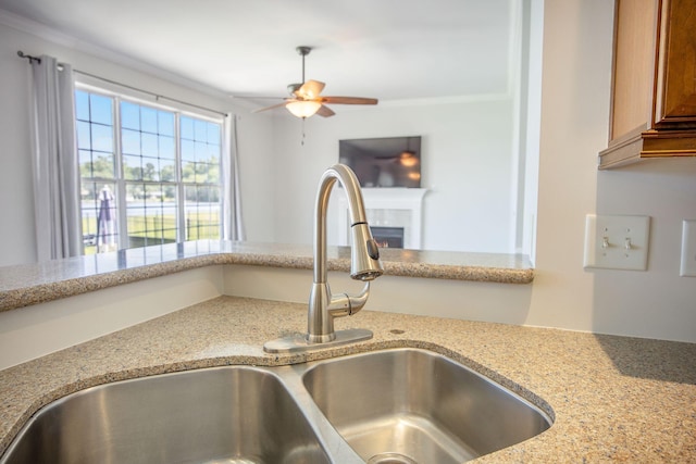 1713 Pimlico Blvd, Moncks Corner, SC 29461 - kitchen view of a sink, a ceiling fan, brown cabinets, a lit fireplace, and light stone countertops