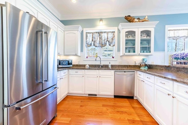 kitchen featuring light wood-style flooring, stainless steel appliances, a sink, white cabinets, and crown molding