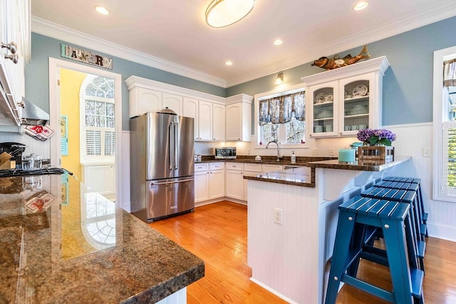 kitchen featuring a peninsula, high quality fridge, white cabinetry, and light wood-style floors