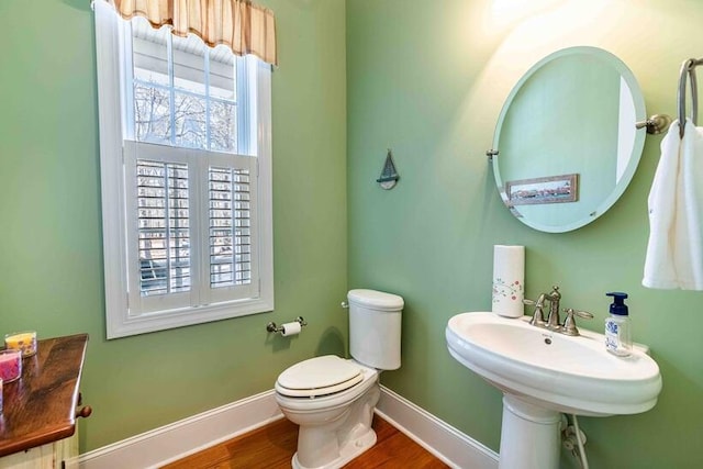 half bathroom featuring wood finished floors, toilet, and baseboards