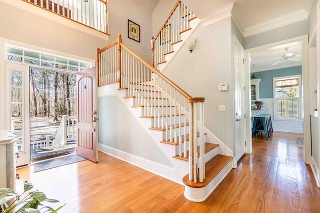 stairs with baseboards, a high ceiling, wood finished floors, and crown molding