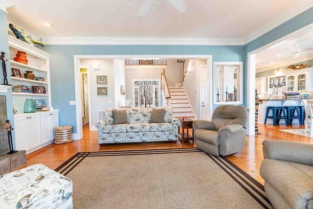 living room with light wood-style floors, crown molding, stairway, and a ceiling fan