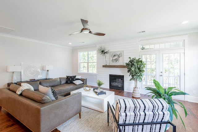 living area with a fireplace, wood finished floors, a ceiling fan, visible vents, and crown molding