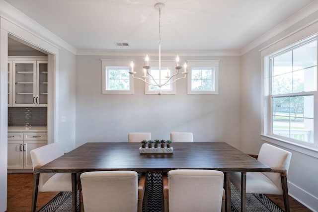 dining space with dark wood-style floors, an inviting chandelier, visible vents, and crown molding