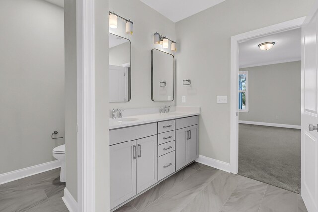 bathroom featuring double vanity, baseboards, toilet, and a sink