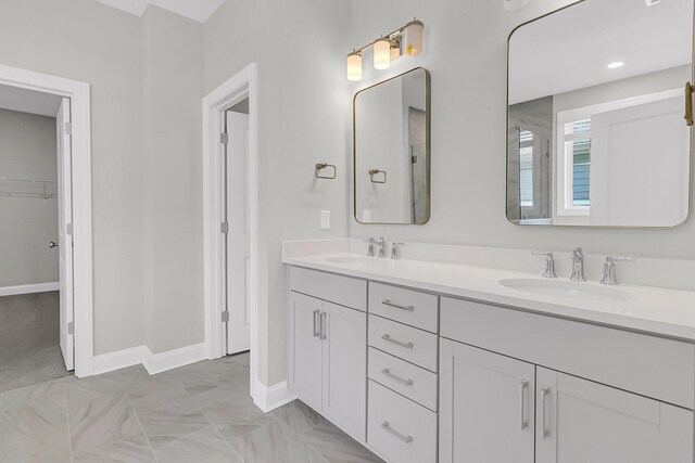 bathroom featuring double vanity, a sink, a walk in closet, and baseboards