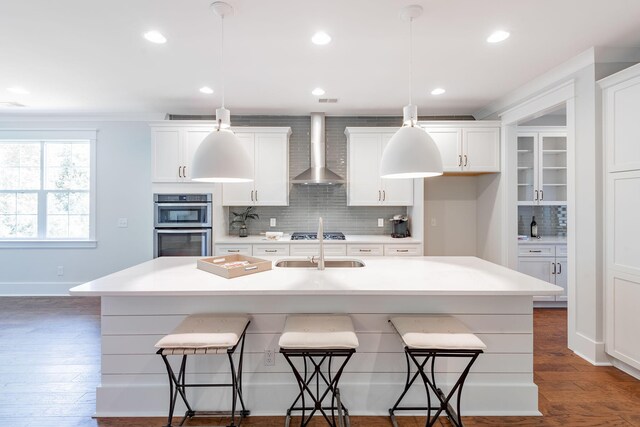 kitchen with a breakfast bar, dark wood-style flooring, white cabinetry, and wall chimney range hood