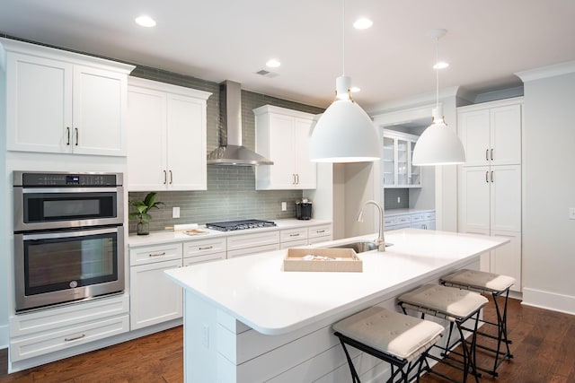 kitchen featuring backsplash, appliances with stainless steel finishes, a sink, an island with sink, and wall chimney exhaust hood