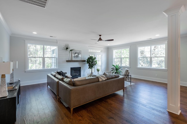 living room featuring dark wood-style floors, ornamental molding, a wealth of natural light, and a glass covered fireplace