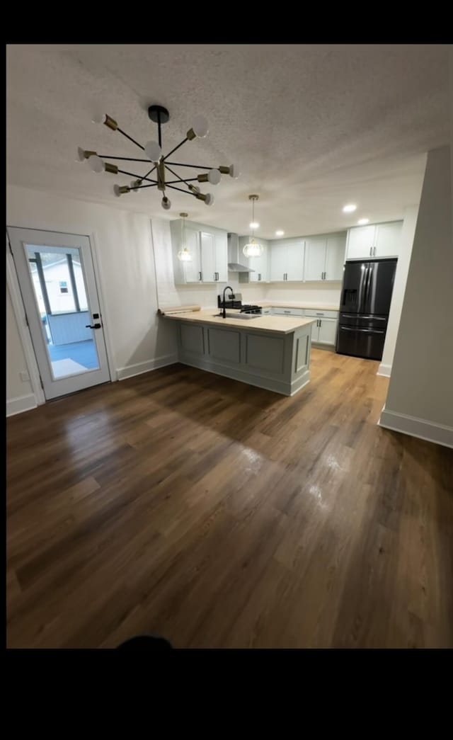 kitchen with dark wood-type flooring, a sink, a peninsula, light countertops, and black refrigerator with ice dispenser