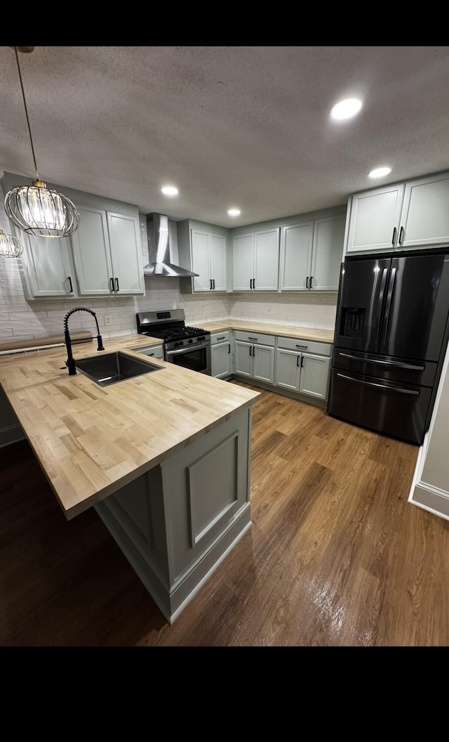 kitchen with a sink, wood counters, black fridge with ice dispenser, wall chimney exhaust hood, and gas range