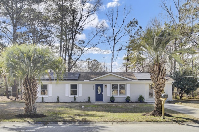 ranch-style home with brick siding, a front yard, and roof mounted solar panels