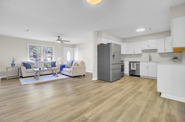 kitchen featuring stainless steel appliances, light countertops, light wood-style floors, open floor plan, and white cabinetry