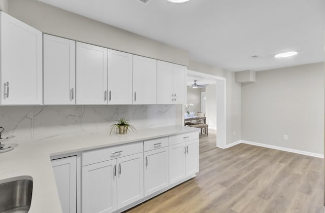 kitchen with light countertops, backsplash, white cabinetry, and light wood-style floors