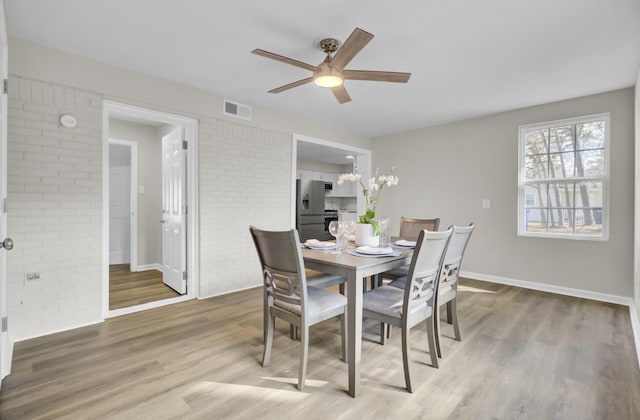 dining area featuring visible vents, baseboards, brick wall, ceiling fan, and light wood-type flooring