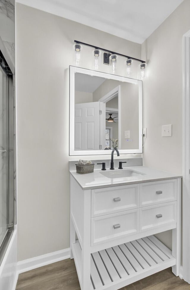 full bathroom featuring baseboards, ceiling fan, wood finished floors, combined bath / shower with glass door, and vanity