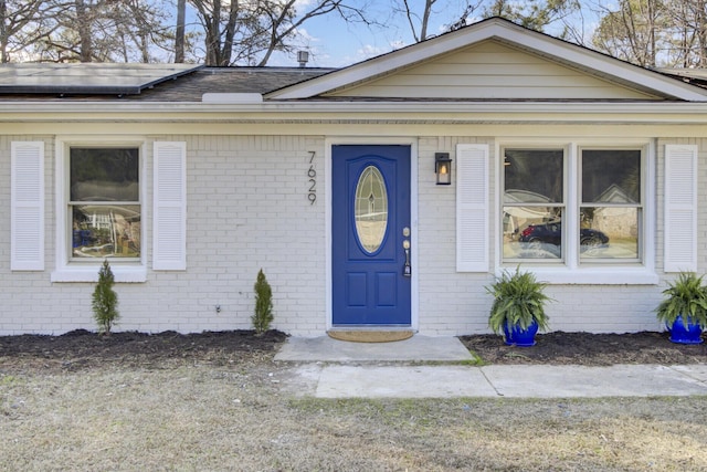 entrance to property featuring roof mounted solar panels and brick siding