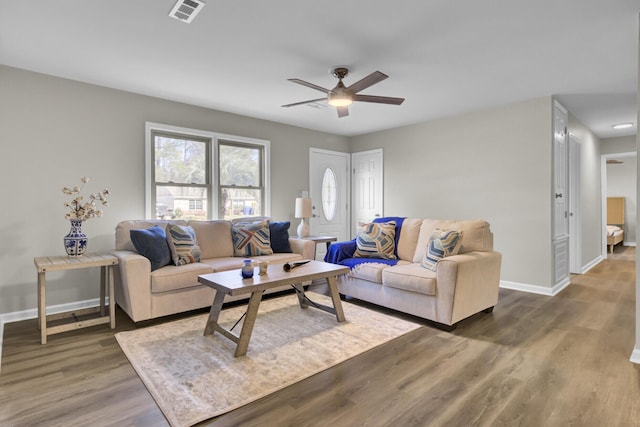 living room with dark wood-style flooring, visible vents, ceiling fan, and baseboards