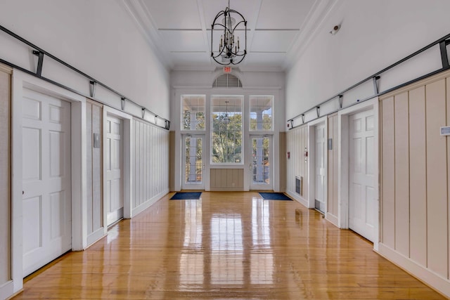 entryway with a towering ceiling, ornamental molding, a chandelier, and light hardwood / wood-style floors