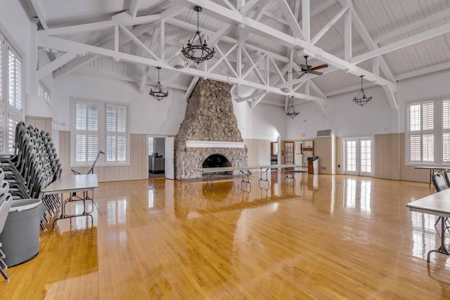 living room with high vaulted ceiling, ceiling fan with notable chandelier, a stone fireplace, beam ceiling, and hardwood / wood-style flooring