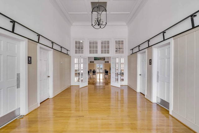 foyer entrance featuring an inviting chandelier, ornamental molding, a towering ceiling, light hardwood / wood-style floors, and french doors