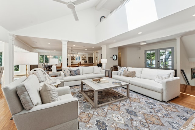 living room with beam ceiling, ceiling fan with notable chandelier, light hardwood / wood-style floors, and high vaulted ceiling