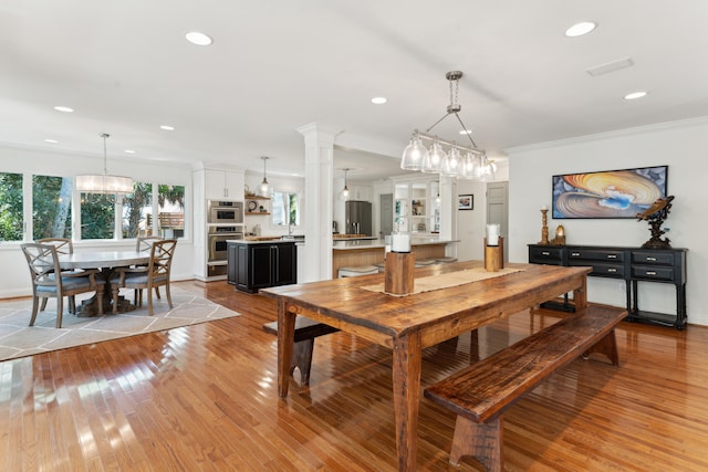 dining area featuring decorative columns, ornamental molding, sink, and light hardwood / wood-style flooring