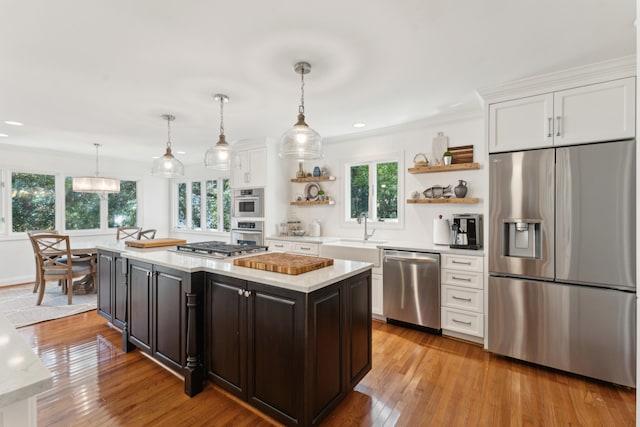 kitchen with light hardwood / wood-style floors, white cabinetry, stainless steel appliances, and hanging light fixtures