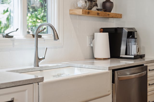 kitchen featuring stainless steel dishwasher, light stone countertops, white cabinetry, and sink