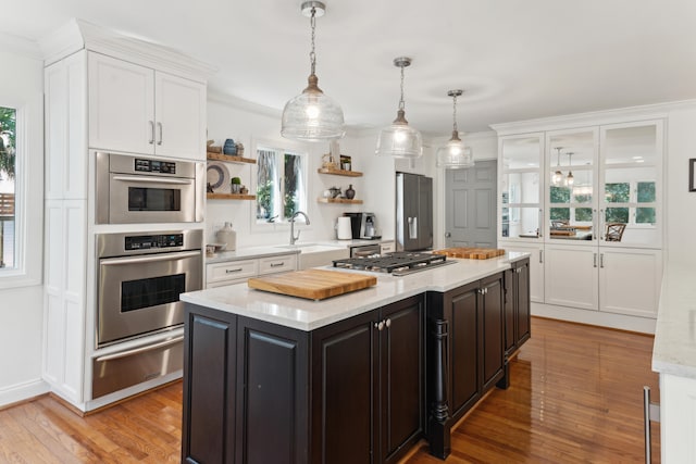 kitchen with sink, hanging light fixtures, stainless steel appliances, light hardwood / wood-style flooring, and a kitchen island