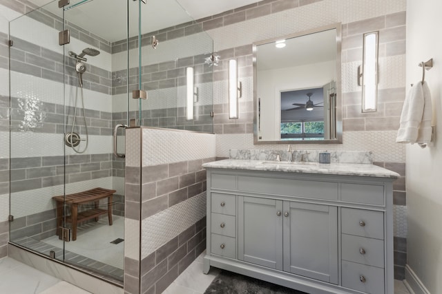 bathroom with ceiling fan, tile patterned floors, an enclosed shower, vanity, and tile walls