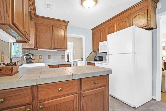 kitchen featuring visible vents, a sink, brown cabinets, and white appliances