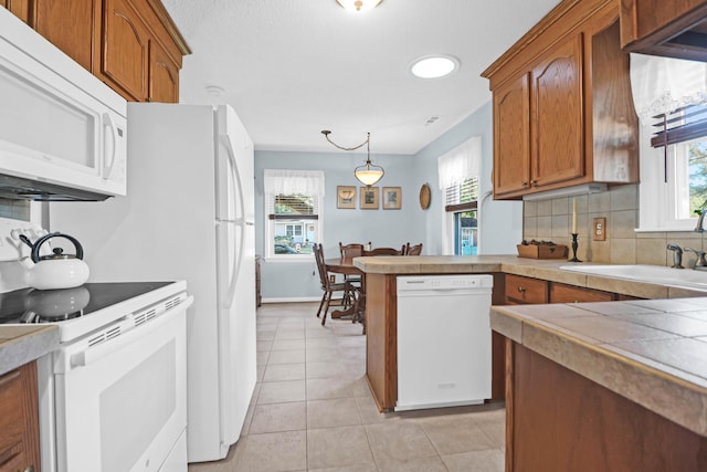kitchen with tasteful backsplash, a peninsula, brown cabinets, light tile patterned floors, and white appliances