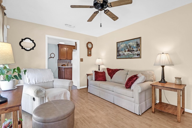 living room featuring light wood finished floors, baseboards, visible vents, and a ceiling fan