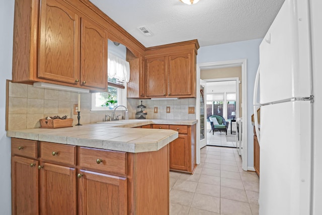 kitchen featuring light tile patterned floors, a sink, visible vents, freestanding refrigerator, and brown cabinets