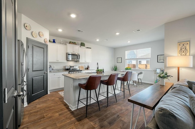 kitchen with a center island with sink, white cabinetry, a kitchen breakfast bar, stainless steel appliances, and light stone counters