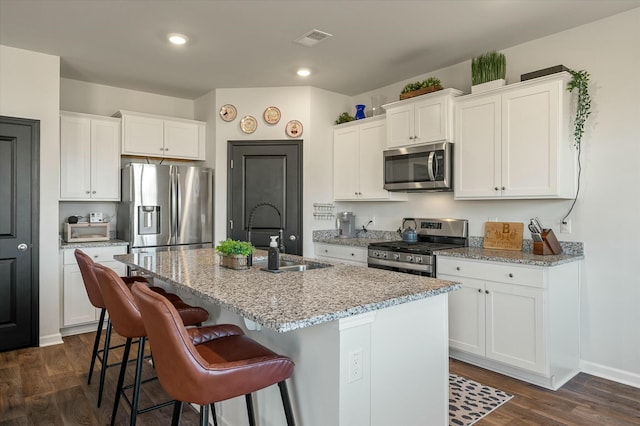 kitchen with stainless steel appliances, sink, white cabinets, and a kitchen island with sink