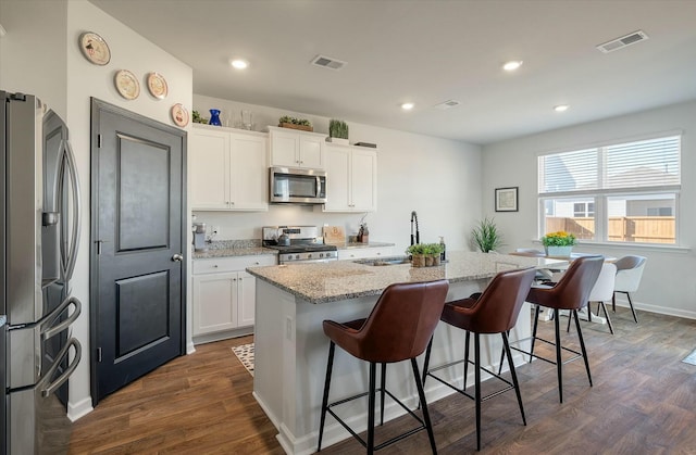 kitchen featuring dark wood-type flooring, appliances with stainless steel finishes, white cabinets, and an island with sink