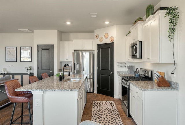 kitchen featuring sink, a kitchen island with sink, stainless steel appliances, white cabinets, and light stone counters