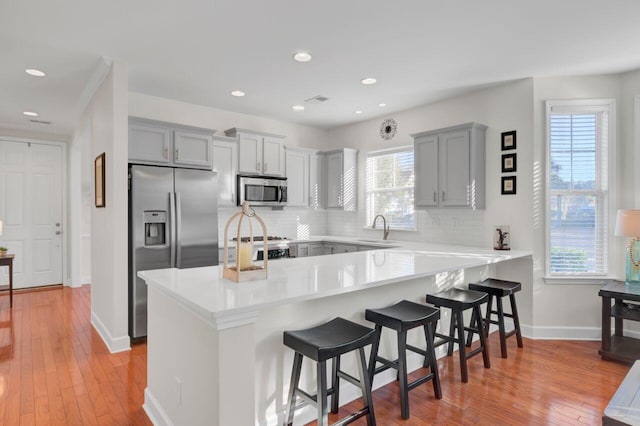 kitchen featuring sink, kitchen peninsula, decorative backsplash, a breakfast bar, and appliances with stainless steel finishes