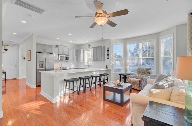 living room with ceiling fan, plenty of natural light, sink, and light wood-type flooring