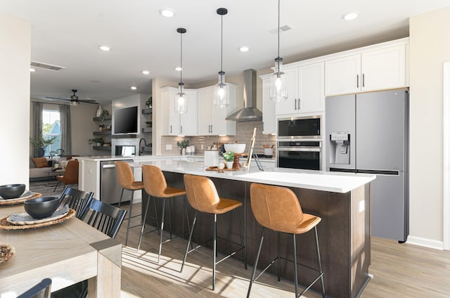 kitchen featuring wall chimney exhaust hood, stainless steel appliances, ceiling fan, pendant lighting, and white cabinetry