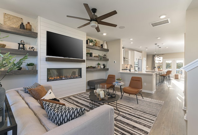 living room featuring ceiling fan, sink, a fireplace, and light hardwood / wood-style flooring