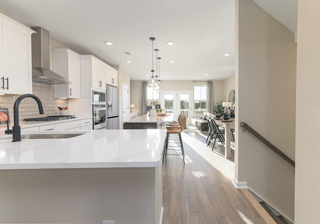 kitchen featuring white cabinetry, wall chimney exhaust hood, stainless steel appliances, pendant lighting, and light hardwood / wood-style floors