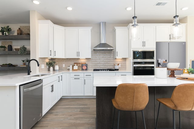 kitchen with stainless steel appliances, wall chimney range hood, wood-type flooring, white cabinets, and hanging light fixtures